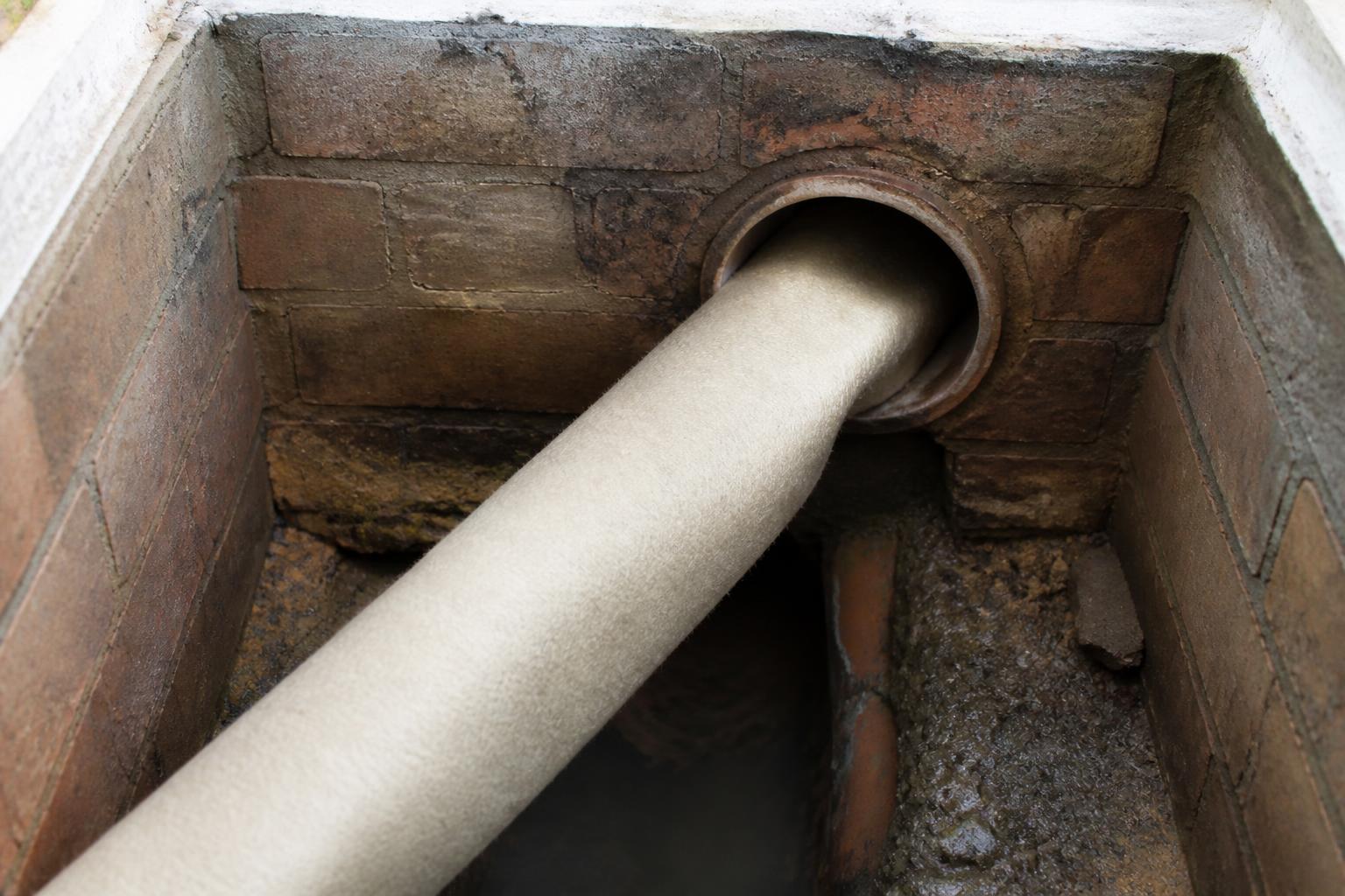 Cured-in-place pipe (CIPP) liner being inverted into a damaged clay drain at an open brick manhole — no-dig drain lining