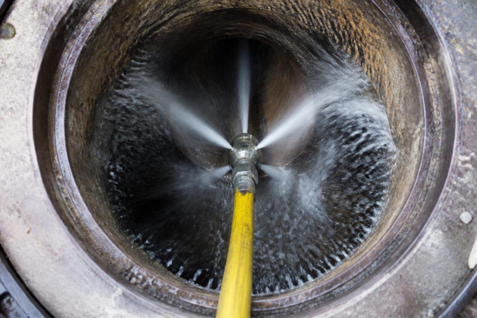 High-pressure water jetting nozzle clearing the interior of a blocked underground drainage pipe